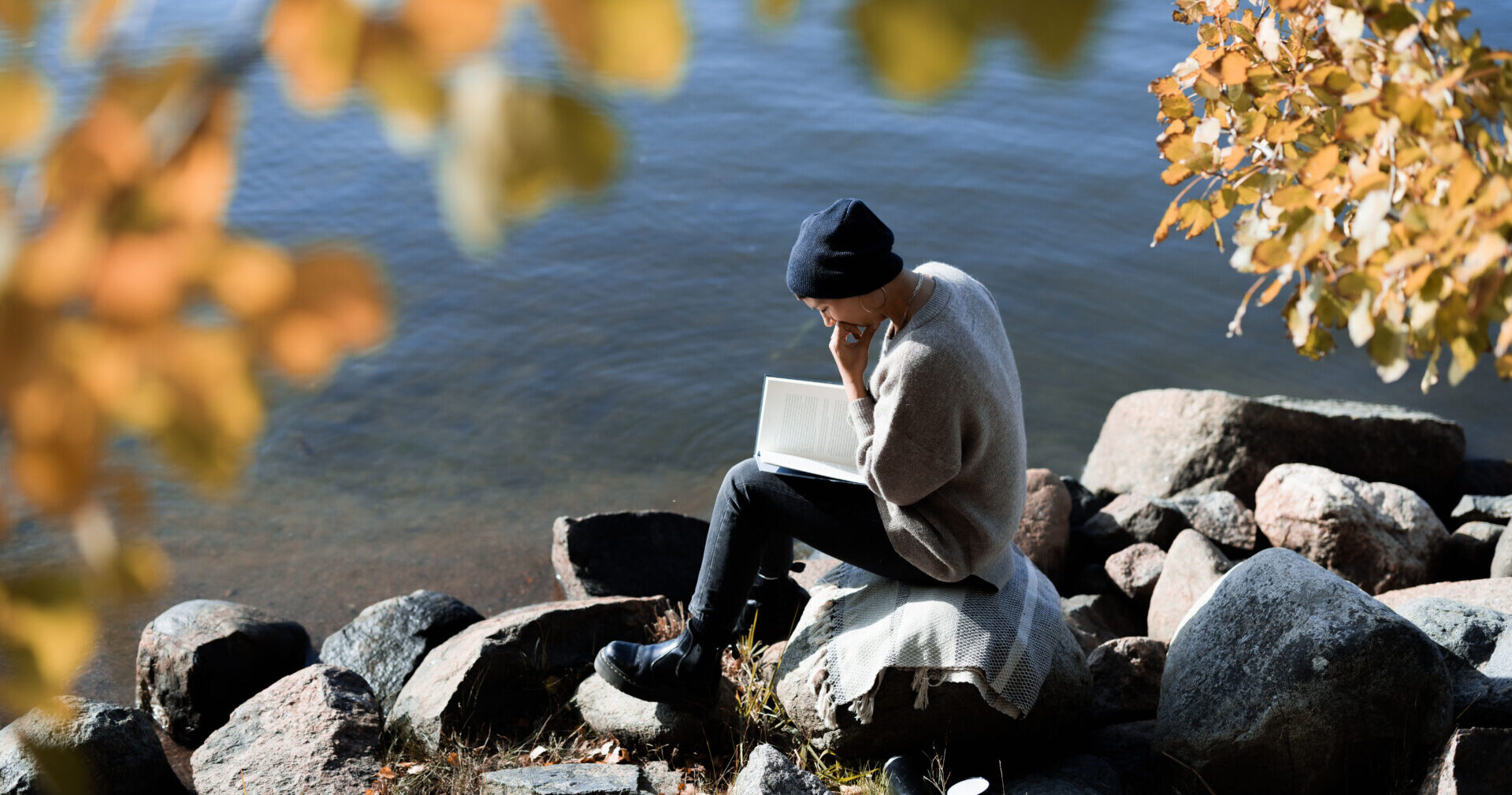 Henkilö lukee meren äärellä.